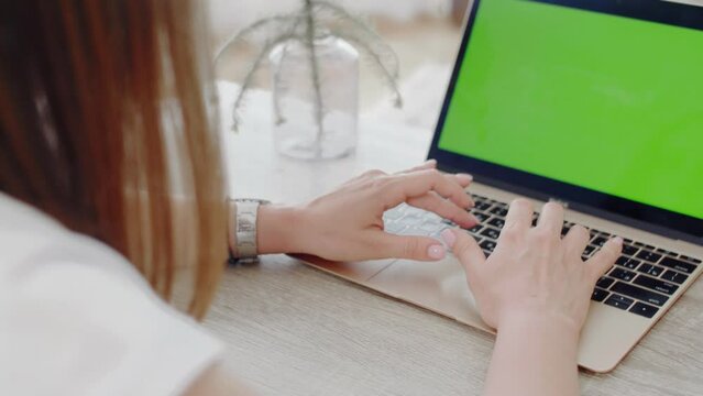 A young dark-haired woman working on a laptop with a green screen background is captured in 4K video footage, POV from her shoulder