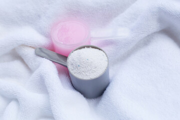 Detergent powder and fabric softener in measuring spoon on towel. Laundry concept.