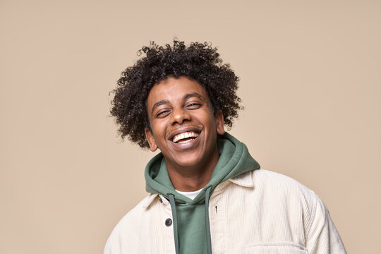 Happy joyful young African American hipster guy isolated on beige background. Smiling funny ethnic teen student, cool curly gen z fashion model laughing with dental smile white teeth, portrait.