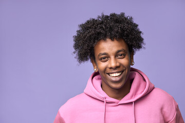 Young happy hipster African American teen guy wearing pink hoodie isolated on purple background. Smiling cool ethnic generation z teenager student model standing looking at camera posing for portrait.