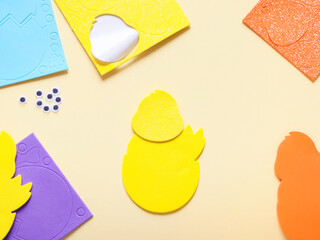 Colored felt set of yellow chicken and patterned stickers lying on the sides on a pale yellow
