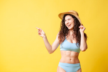 young curly brunette girl in a blue swimsuit in the summer shows her hands to the side on the copy space and smiles