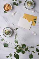 Greeting card mockup background. Mint green postal envelope, blank white card, pen and office stationary. Silver dollar eucalyptus twigs on stone, overhead view. Copy-space, place for text, lettering.