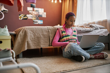 Black teenage girl using laptop indoors sitting on floor