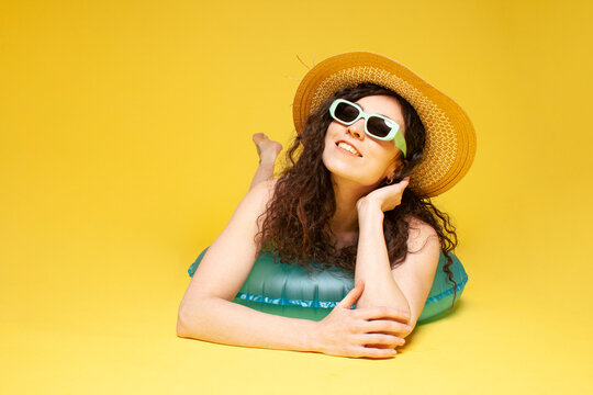 young girl in straw hat lies on inflatable swimming circle on yellow background and smiles, woman in sunglasses
