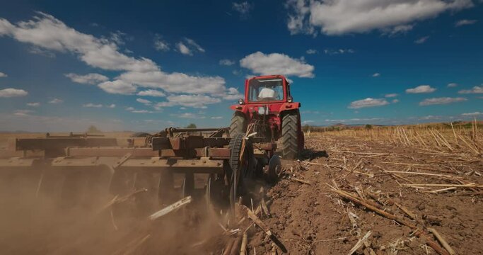 Farmer in tractor harrowing the ground in a agricultural field. Cultivate, agriculture and farming concept in 4k video