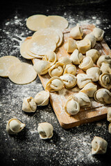 Raw dumplings and round pieces of dough on a cutting board. 