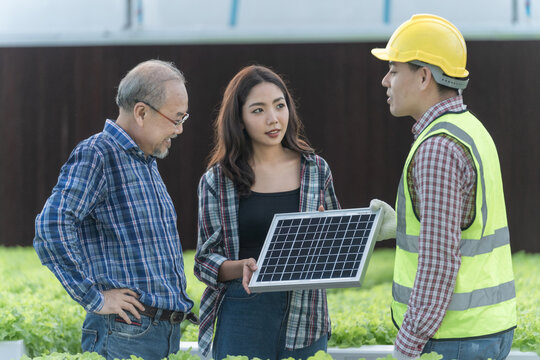 Engineers man inspecting a solar panel device for greenhouse for cultivation of vegetable food. Senior farmer and worker talking to choose high efficiency photovoltaic panel for renewable energy.