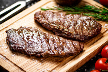 Grilled steak on a cutting board with rosemary and tomatoes. 