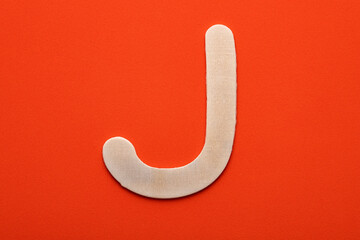 Alphabet letter J - White wood piece on orange foamy background