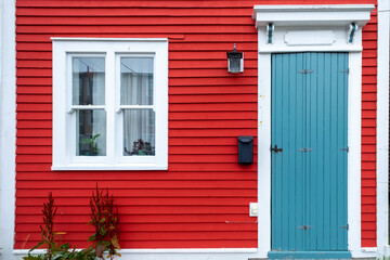 A bright red wooden exterior wall of a country style house. The building has red narrow wood clapboard cape cod siding.  It has a small wooden door, a double pane glass window, and a black mailbox.
