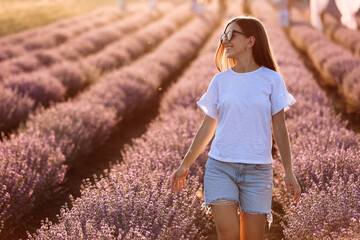 Beautiful young woman walk and look on the lavender field on sunset light. girl in sunglasses...