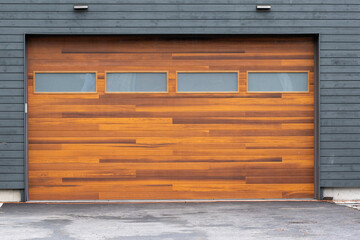 A modern brown faux wooden exterior garage door with four small horizontal glass windows. The...