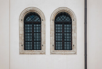 Fototapeta na wymiar Two antique old windows with black iron bars framed on a light grey wall. The Jesuit Church in Lviv.