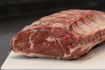 A large rack of raw beef prime rib on a brown industrial plastic cutting board. The meat is sitting on the kitchen counter of a restaurant prior to being cut into prime rib steaks for barbequing. 