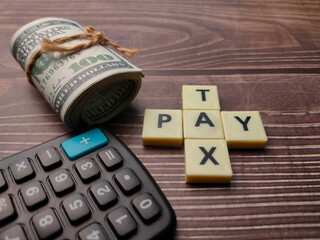 Banknotes and calculator with the word TAX PAY or PAY TAX on wooden background.