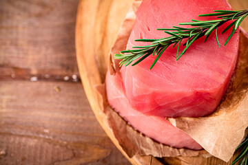 A steak of raw tuna on a cutting board with a sprig of rosemary. 