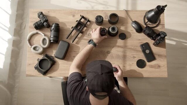 Top down view of desktop where videographer clean dust and dirt from equipment. man in cap work with lens from photo camera or video camera. photographer takes care of equipment. Lens repair service.