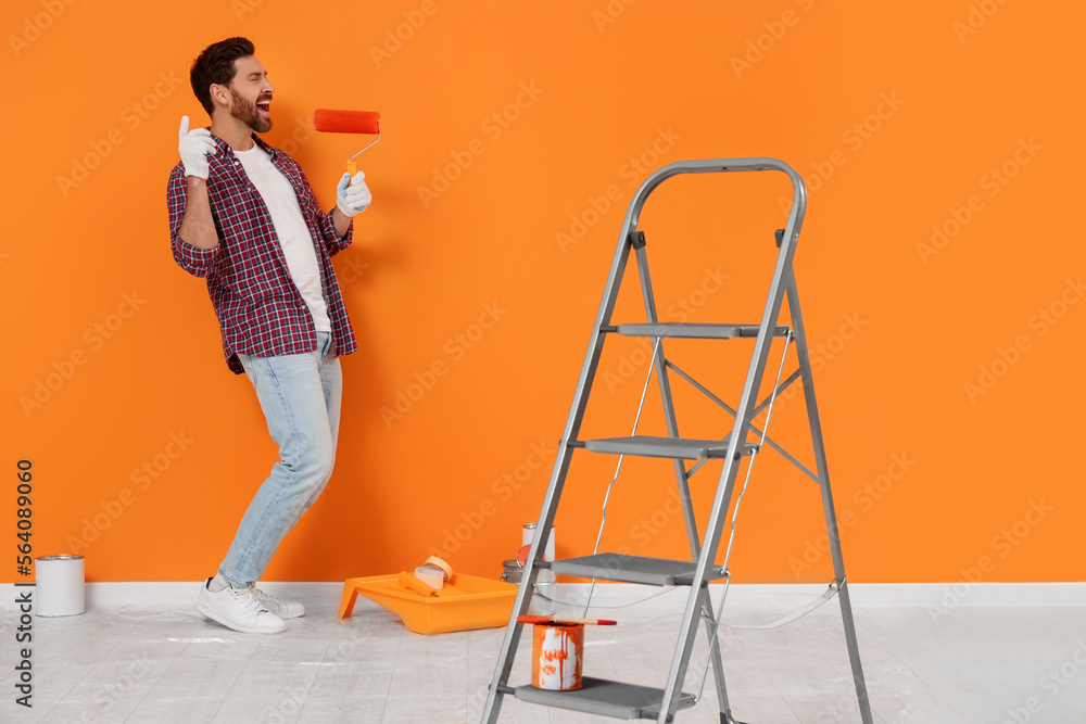 Wall mural Emotional designer with roller and painting equipment near freshly painted orange wall indoors