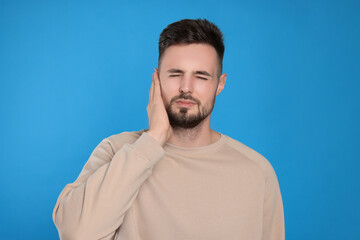 Obraz premium Young man suffering from ear pain on light blue background