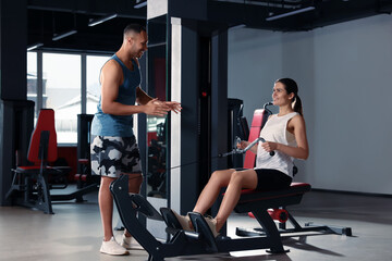 Fototapeta na wymiar Happy trainer explaining woman how to do exercise properly in modern gym