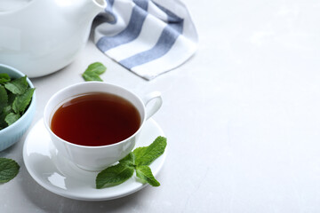 Cup with hot aromatic mint tea on light table, space for text