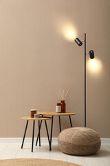 Knitted pouf, lamp and decor elements near beige wall indoors. Space for text