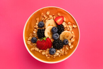 Delicious smoothie bowl with fresh berries, banana and oatmeal on pink background, top view