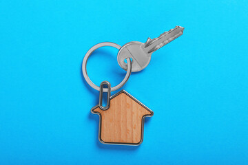 Key with trinket in shape of house on blue background, top view. Real estate agent services