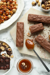 Tasty chocolate bars with caramel and nuts on white marble table, flat lay