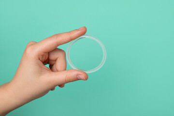 Woman holding diaphragm vaginal contraceptive ring on turquoise background, closeup. Space for text
