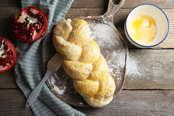 Homemade braided bread and ingredients on wooden table, flat lay. Cooking traditional Shabbat...