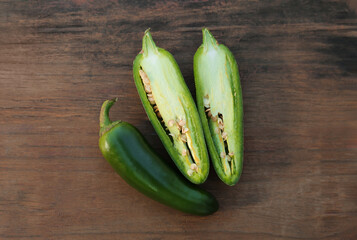 Whole and cut green chili peppers on wooden table, flat lay