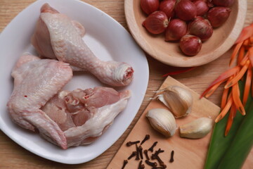 Flat lay pieces of raw chicken meat with some kitchen spices such as shallots, garlic, and cloves on the kitchen table