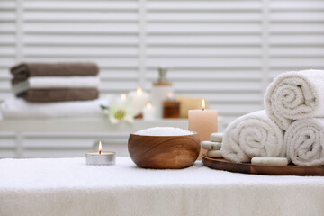 Fototapeta na wymiar Spa composition with rolled towels and burning candles on massage table in wellness center, space for text