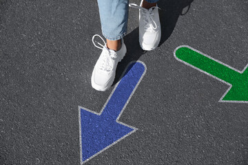 Choice of way. Woman walking to drawn mark on road, closeup. Green and blue arrows pointing in different directions