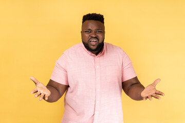 Portrait of unhappy stressed man wearing pink shirt standing raised arms and asking, expressing...