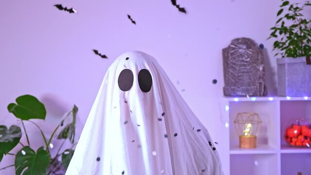 White ghost costume for Halloween party with neon lights in the background. The ghost is celebrating Halloween. A ghost at a confetti party. Portrait of a ghost. The monster is celebrating Halloween.