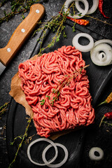 Raw minced meat on a cutting board with thyme and onion rings. 