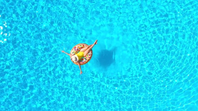 Top down view of a woman in yellow swimsuit lying on a donut in the pool
