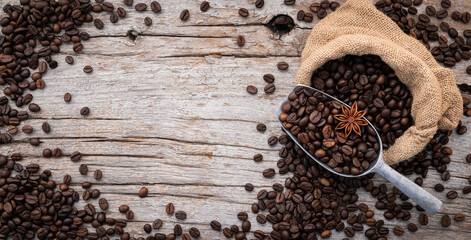 Background of dark roasted coffee beans with scoops setup on wooden background with copy space.