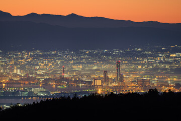 Lights from city mix with orange dawn glow over distant mountains