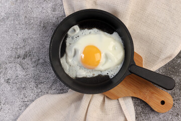 Sunny-Side Up Fried Eggs on a Cast-iron pan on a small cutting board on a dark grey background. Top view, flat lay