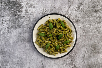 Fusilli pasta with Spicy Pesto and fresh basil leaves on a round plate on a dark gray background. Top view, flat lay