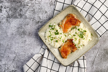 Pan fried chicken thighs with rice and herbs on a white square  plate on a dark background. Top view, flat lay