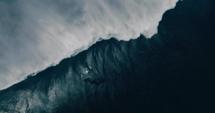 Aerial shot above giant blue ocean wave crashing 