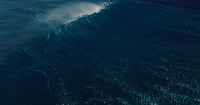 Aerial shot above giant blue ocean wave crashing 