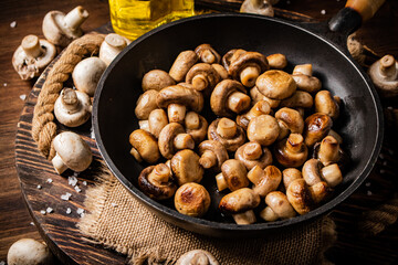 Frying pan with fried mushrooms on a wooden tray. 