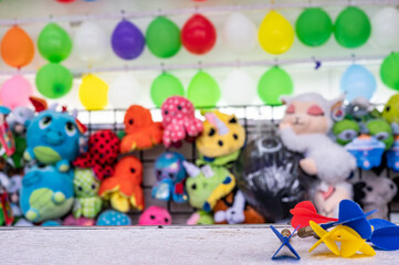 selective focus on darts sitting on a ledge with a wall of balloon targets and prizes that a player can win at a fair.