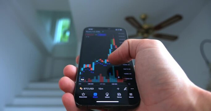 Crypto enthusiast using smartphone app analyzing financial data stock market price on smartphone checking online trading platform application, buying cryptocurrency investments on home office interior